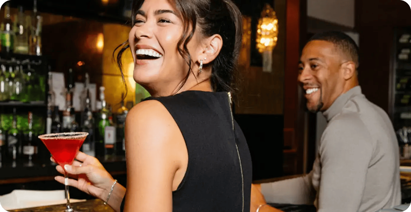 Two guests laughing together at the bar during happy hour